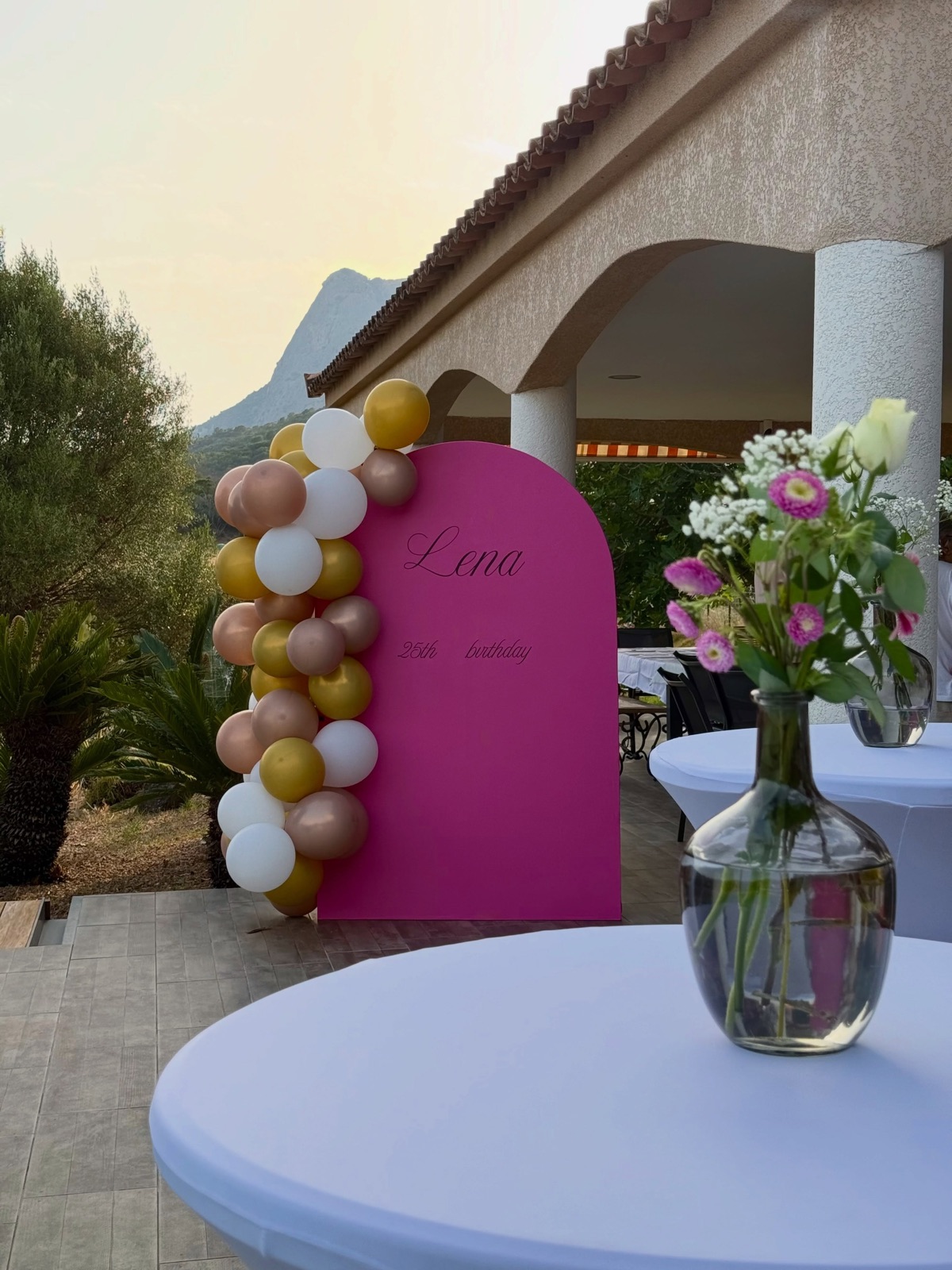 Table haute habillée de blanc avec bouquet de fleurs, arche fuchsia en fond